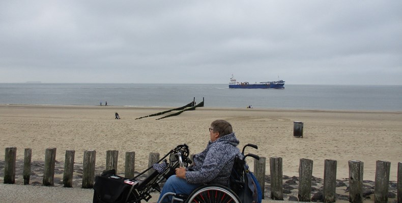 een vrouw rijdt in een rolstoel naast het strand.