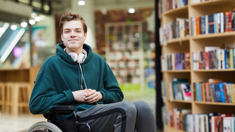 Een jongen zit in een rolstoel in een bibliotheek.